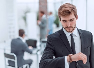 Ofiste duran ciddi bir iş adamı ve kol saatine bakıyor.