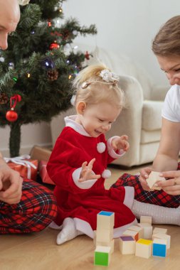 Toddler child with cochlear implant plays with parents under christmas tree - deafness and innovating medical technologies for hearing aid