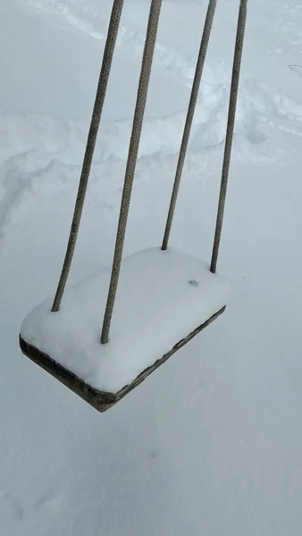 4本のロープで子供たちの木製のスイングは雪で覆われています — ストック写真