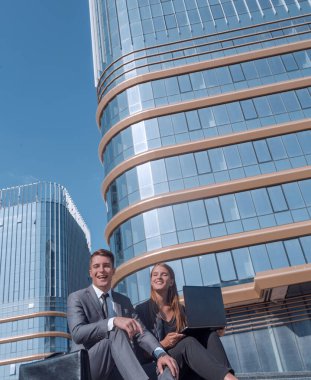 İş gününden sonra iş merkezinin önünde dizüstü bilgisayarlı genç çalışanlar oturuyor.