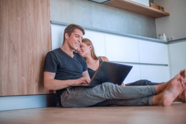 Genç çift yeni bir dairenin zemininde dizüstü bilgisayar kullanıyor.