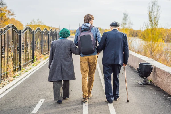 老夫婦は 男性アシスタントまたは大人の孫と公園を散歩します ボランティア活動 高齢者のケア — ストック写真