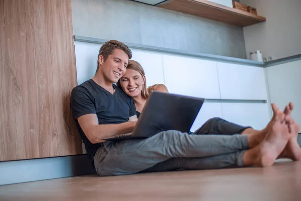 年轻夫妇坐在新公寓的地板上使用笔记本电脑 — 图库照片