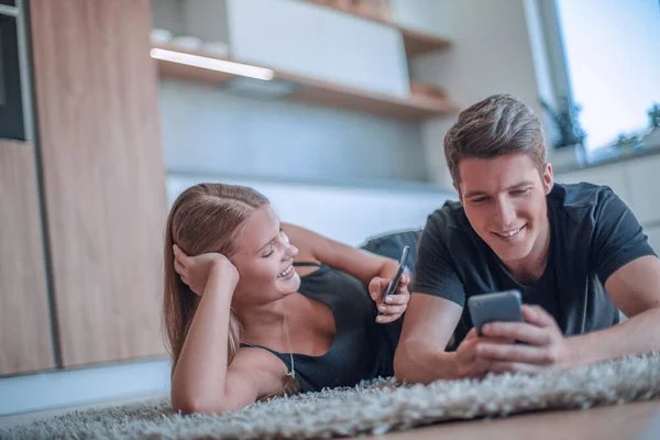 年轻夫妇在新公寓的地毯上放着智能手机 — 图库照片
