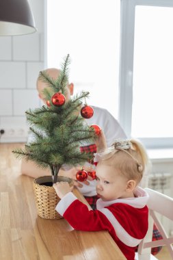 Child with cochlear implant hearing aid having fun with father and small Christmas tree - diversity and deafness treatment and medical innovative technologies