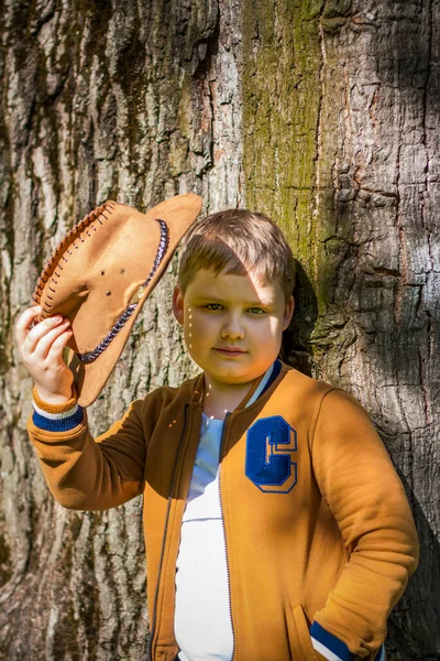 Söt Pojke Poserar Cowboyhatt Skogen Vid Ett Träd Solens Strålar — Stockfoto