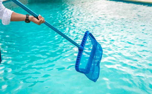 葉のスキマーで男の掃除プール スキマーでプールを掃除する男スキマーでプールを掃除する人手を背景に青いプールでスキマーを保持 — ストック写真