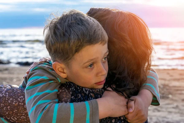 かわいい悲しい少年は夕日の海に母親を抱きかかえて — ストック写真