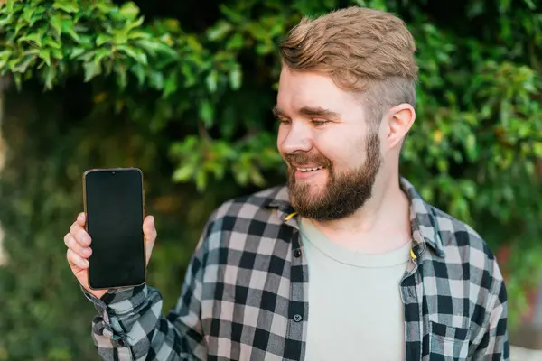 Happy Bearded Man Showing Blank Smartphone Screen Green Leaves Background — Stock Fotó