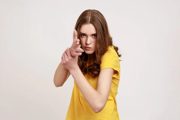 我会杀了你身穿黄色T恤 怒气冲冲的少女的画像 用手指指着相机 威胁要开枪 用手模仿武器 — 图库照片