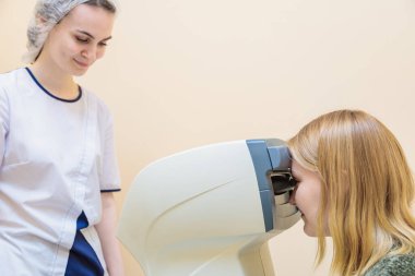 A girl optometrist examines the eyes of a patient using special modern equipment