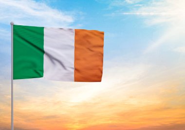 Bayrak direğine uzanan 3 boyutlu bir İrlanda bayrağı ve arka planda gün batımlı güzel bir gökyüzü.