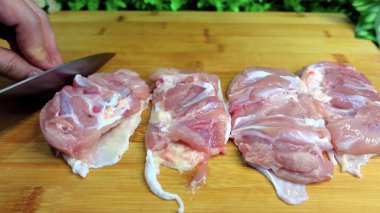 Female hands cut chicken fillet on a wooden board