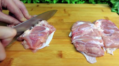 The cook cuts raw chicken into pieces on a cutting board.