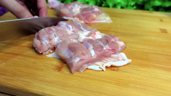 Fresh chicken meat is cut with a knife on a wooden board,