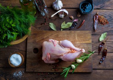 Mutfak tahtasındaki çiğ tavuk, yeşiller, tuzluk ile tuz, biber, sarımsak, yeşil ve kırmızı biber ahşap arka planda..