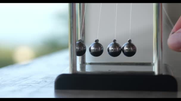 一只手的特写驾驶一个简单的牛顿摇篮 色彩斑斓的金属球摇晃缓慢 惯性概念 — 图库视频影像