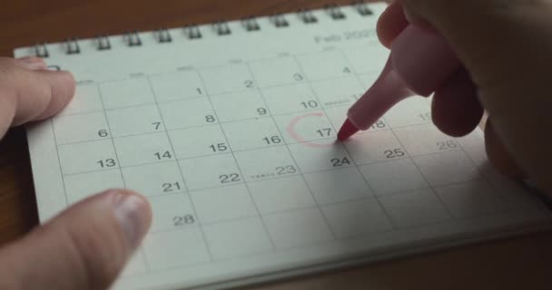 赤いマーカーまたはフェルト先端ペンを使用して手を閉じて カレンダー内の重要な一日を旋回します カレンダーに1日署名する — ストック動画