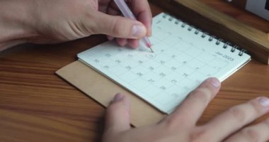 Yakından tanınmayan bir adamın eli kırmızı kalemle, 2023 yılının yeni yıl takviminde önemli bir tarihi vurgular.