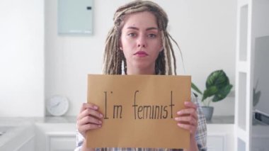 Ciddi bir kadın ofiste feminist posteriyle dikilip kameraya bakıyor. Feminizm ve cinsiyet eşitliği kavramı