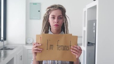Ciddi bir kadın ofiste feminist posteriyle dikilip kameraya bakıyor. Feminizm ve cinsiyet eşitliği kavramı