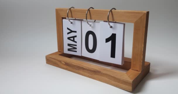 白い壁の背景に対する机の永久カレンダーの5月1日 春休み 国際労働者の日 — ストック動画