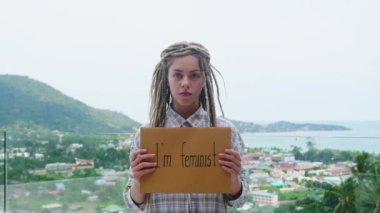 Ciddi bir kadın feminist bir posterle duruyor ve kameraya bakıyor. Feminizm ve cinsiyet eşitliği kavramı