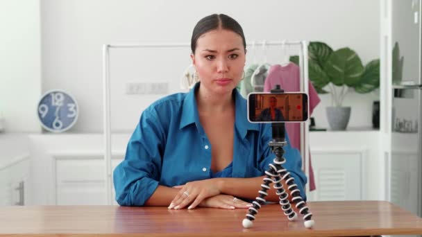 女性はリビングルームで一人ソファに座ってスマートフォンを使用してビデオVlogを記録し 三脚の上にデバイスを置きます女性フィルム新しいVlogは オンラインライブストリームを作ります リードウェビナー遠いチャット 現代の技術ビデオイベント — ストック動画