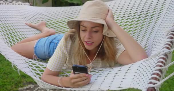 Lachende Blonde Vrouw Met Een Zonnebril Met Smartphone Ontspannen Liggend — Stockvideo