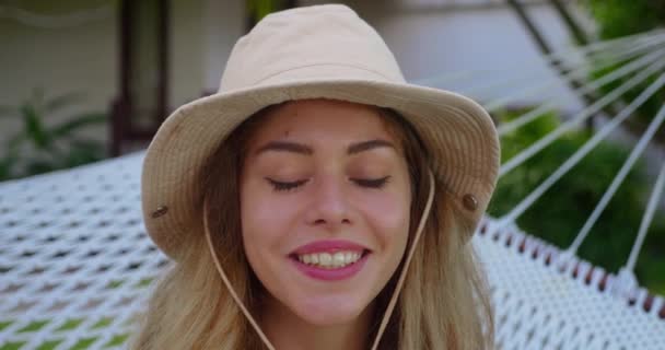 帽子をかぶった愛らしい女の子がカメラを見て笑っている カジュアルな服装で笑顔の女性の閉じる屋外に座っています — ストック動画