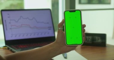 Yeşil renkli ekran krom anahtarı olan bir kadın cep telefonu çalışma alanı arkaplanının akıllı telefonunu tutar. Hisse büyümesi konsepti, iş. Başarılı satış stratejisi.