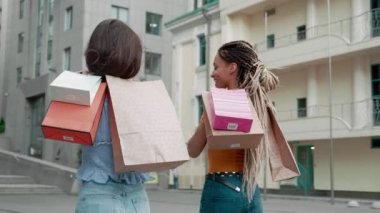 Two female friends are walking down the street outdoors after shopping. African American and Asian woman after shopping. Back view. friends hold packages with new purchases. Shopping concept.