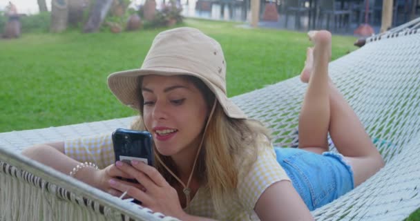 Woman Hat Lies Hammock Holds Smartphone Surprised Woman Vacation Says — Stockvideo