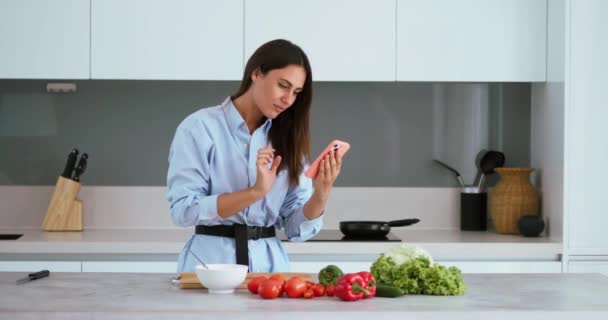 Kobieta Gospodarstwa Smartfon Patrząc Ekranie Sprawdza Listę Vegies Gotować Domu — Wideo stockowe