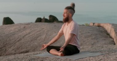 Tıraşlı şakakları olan bir adam taşın üzerinde oturur. Ruhsal gelişim kavramı. Adam Zen 'i yakalıyor ve ruhsal gelişimi kavrıyor. Şafak vakti gökyüzüne bakan adam Lotus pozisyonunda meditasyon yapıyor. Ruhsal gelişim..