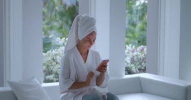 Spa 'dan sonra rahatlayan kadın beyaz havlu konseptiyle oturur. Kişisel zaman dilimi. Genç kadın kişisel mesaj yazar..