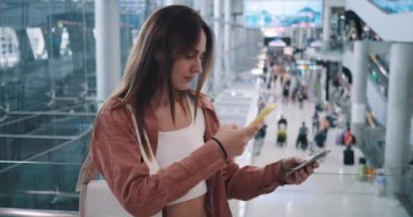 Havaalanının arka planında duran kadın elinde akıllı bir telefonla turist seyahati konseptini tarıyor. Kadın kapılarını, koltuklarını ve ayrıcalıklarını kontrol ediyor. Turist seyahati..