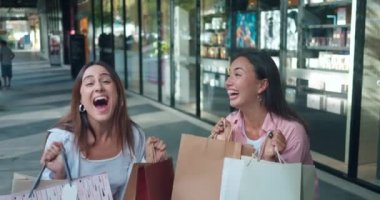 Alışveriş merkezindeki kadınlar, alışveriş torbaları sergilerler ve canlı duyguları ön plana çıkarırlar. Kadınların duyguları mutluluk alışveriş yapan kadınların duygularıyla birleşir. Samimi neşe zarafeti.
