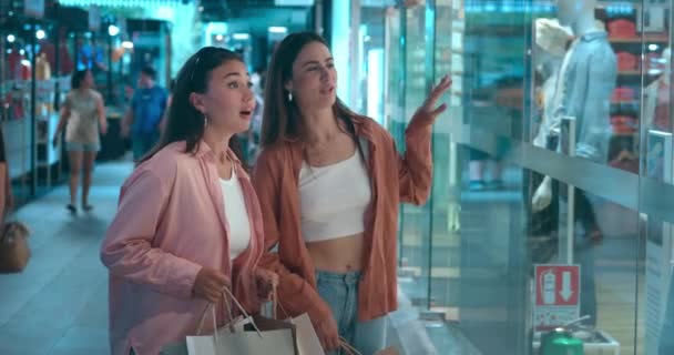 购物中心的两名妇女正在观看讨论潜在采购的陈列柜 展示会引发关于新衣服的快乐对话展示会购物快乐消费的游乐场 — 图库视频影像