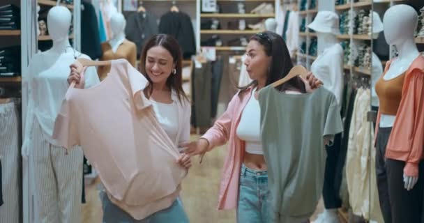 友人は 流行の衣装を選択するモールのショッピング衣料品店を楽しんでいます 女性のショッピングは現代のライフスタイルの幸福を象徴しています ショッピング シンボル繁栄 美しい選択 — ストック動画