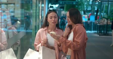 Alışveriş merkezinin vitrinlerine bakan kadınlar mağazaların vitrinlerini tartışıyor moda neşesi sergiliyorlar. Mutlu hayatın aynaları şık kıyafetler moda keşiflerini kucaklıyor.