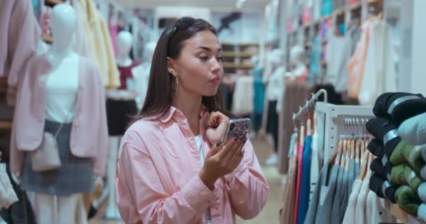 服のなかで女性は 携帯電話やショッピングでテキストを送りながら楽しむことができ 現代の技術に精通したショッピングを反映しています ファッショナブルアイテムを選択する喜び シンボル富 ショッピング ミックス スタイル テクノロジー — ストック動画