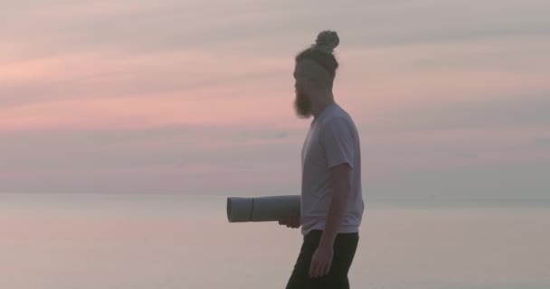 海を見ている手で運動マットを持つ男性の孤独な考察の背景 自然の中で調和を求める大きな内なる世界の孤独な考え方への孤独な探求の旅 — ストック動画