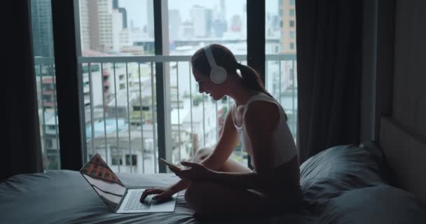 Kvinnan Sitter Sängen Sovrummet Arbetar Laptop Med Hjälp Telefon Musik — Stockvideo