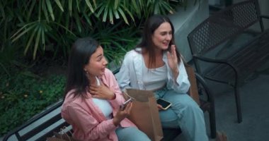 Genç kadınlar bankta oturuyor, telefonları paylaşıyor, kahkahalar atıyorlar. Kahkahalar neşe dostluğu yansıtır. Kahkaha işareti kadınlar dostluğa saygı olumlu titreşimler hayata kucak açan sevinçler.