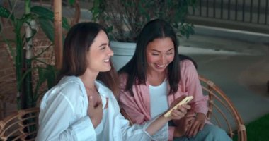 Genç kadınlar bankta oturup sohbet ediyorlar. El ele tutuşuyorlar. Güven dostluğu gösteriyorlar. Güven dostluk gülüşü dostluk temeli neşe dolu hayat paylaşılan pozitifliği kucaklamak