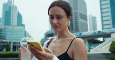 Kadın, Bangkoks 'un arka planında duruyor modern gökdelenler telefonla su içiyor. Bangkok yeni teknolojinin ve Bangkok 'un fütüristik mimarisinin sembolü.