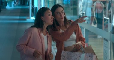 Alışveriş merkezindeki kadınlar canlı bir şekilde alışveriş vitrinlerinde mutluluk kıvılcımları görüldüğünden bahsediyorlar. Yeni kıyafetlerdeki alışveriş mutluluğunun sembolü. Alışverişin heyecanını kucaklayan.