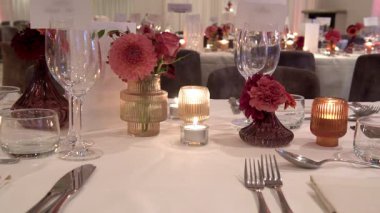 Zarif sofra takımları, renkli cam süsleme parçaları ve şenlikli çiçek düzenlemeleri içeren güzel düzenlenmiş bir yemek masası, şenlikli toplantılar ya da düğün resepsiyonları için uygun..