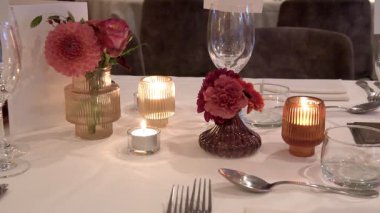 Zarif sofra takımları, renkli cam süsleme parçaları ve şenlikli çiçek düzenlemeleri içeren güzel düzenlenmiş bir yemek masası, şenlikli toplantılar ya da düğün resepsiyonları için uygun..
